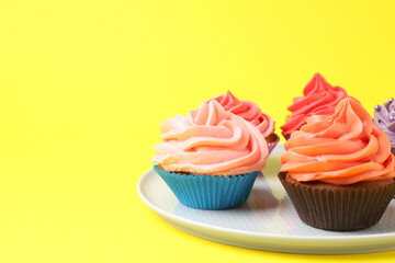 Delicious cupcakes with bright cream on yellow background. Space for text