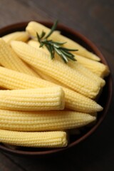 Tasty fresh yellow baby corns in bowl on wooden table, closeup