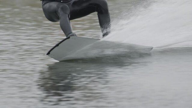 Low section of unrecognizable professional surfer wakeboarding across water at cable park