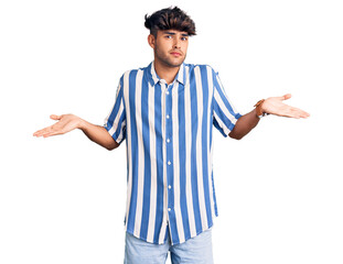 Young hispanic man wearing casual clothes clueless and confused expression with arms and hands...