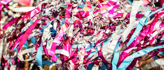 Colorful confetti and streamer lying on floor in fron of background. Festive background of confetti. Trendy neon pink purple blue colored backdrop. Blurred glittered background