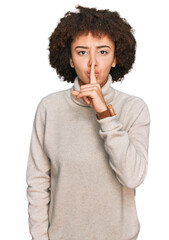 Young hispanic girl wearing wool winter sweater asking to be quiet with finger on lips. silence and...