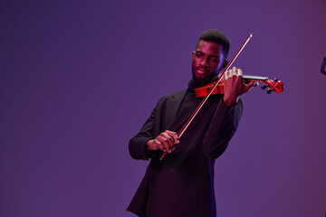 Elegant man playing violin in front of vibrant blue background in formal attire to music