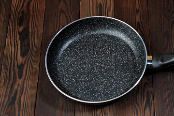 Metal frying pan: Ceramic coating with non-stick coating: Kitchen utensils; On a wooden background:...