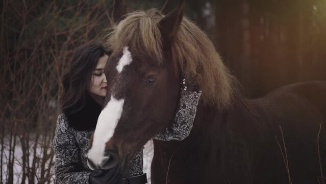 A young brunette cowgirl taking care of mare riding horse while winter season at countryside. Petting domestic animal. A symbol of wild freedom and elegance. Equestrian sport, anilmal love concept.