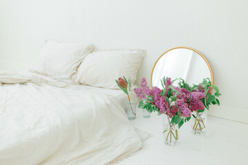 White space with linen bedding golden mirror and white and purple lilac on the floor