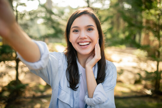 Smiling woman taking selfie in sunlit park