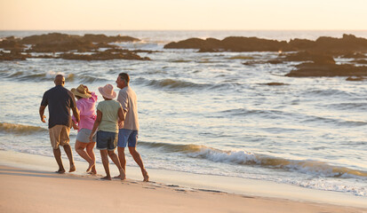 Rear View Of Mature Couple With Friends On Vacation Walking Along Beach Shoreline At Sunset