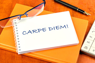 The Latin phrase Carpe Diem, a quote from Horace, means seize the moment. Live in the present written on a clean white notebook