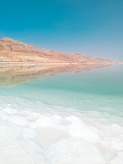 Fototapeta na wymiar Landscape view on Dead Sea salt crystals formations, clear cyan green water and mountains at Ein Bokek beach, Israel