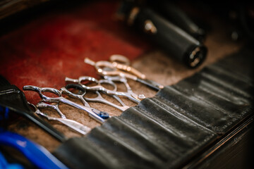 Valmiera, Latvia - Augist 13, 2023 - a close-up of professional hairdressing scissors and clippers neatly arranged in a leather tool roll on a red surface. - obrazy, fototapety, plakaty