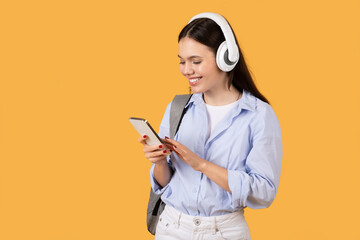Woman focused on smartphone with headphones, yellow background