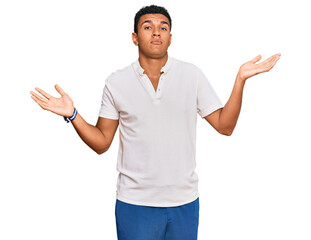 Young arab man wearing casual clothes clueless and confused expression with arms and hands raised....