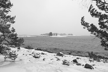 Black and white rocky seashore landscape in cloudy winter weather with snow on the ground, Kopparnäs, Finland.