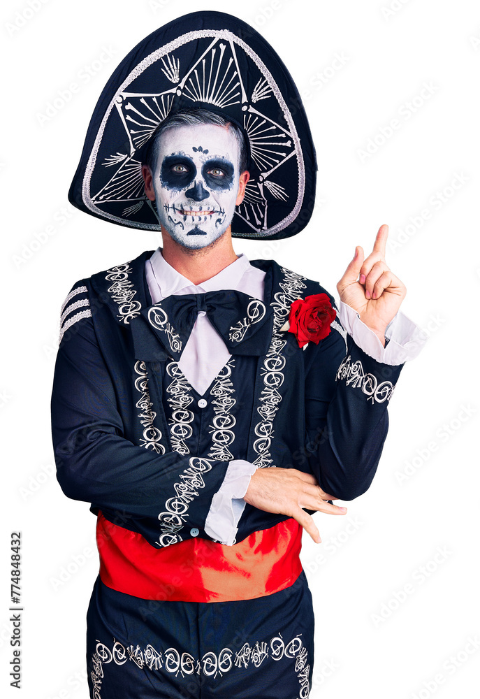 Wall mural Young man wearing day of the dead costume over background with a big smile on face, pointing with hand and finger to the side looking at the camera.