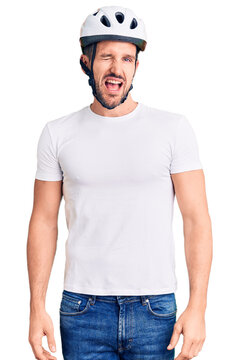 Young handsome man wearing bike helmet winking looking at the camera with sexy expression, cheerful and happy face.