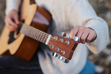 Female guitarist fixing the strings on her musical instrument, close up. Playing the guitar in nature on a cool autumn day