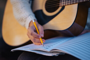 Woman's hand writing notes in her notebook while playing the guitar, close up. Concept of making...