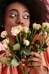 african american woman in peach fuzz outfit holding flowers and looking away on pink backdrop