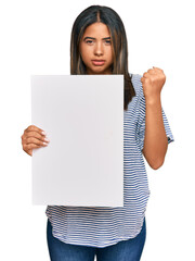 Young latin girl holding blank empty banner annoyed and frustrated shouting with anger, yelling crazy with anger and hand raised