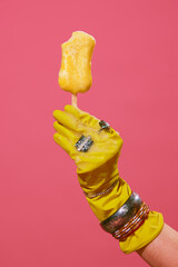 Female hand in rubber cleaning yellow gloves with jewelry, accessories holding melting ice cream...