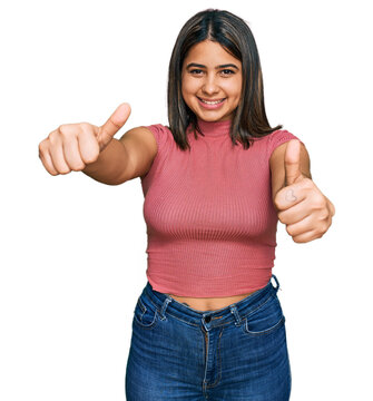 Young hispanic girl wearing casual t shirt approving doing positive gesture with hand, thumbs up smiling and happy for success. winner gesture.