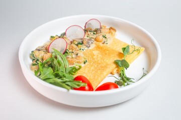 Savory crepe with creamy mushroom sauce and fresh greens on a white plate