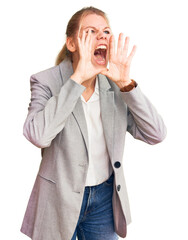 Young beautiful blonde woman wearing elegant jacket shouting angry out loud with hands over mouth