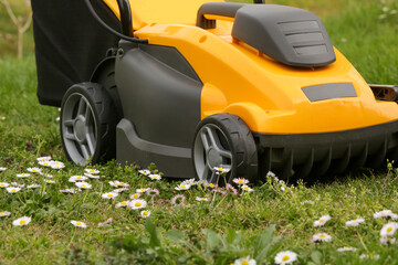Yellow lawn mower on the spring green grass in the yard