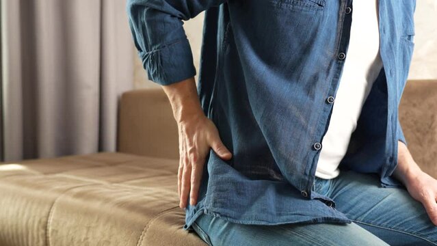 Man sitting on couch and holding his back feels back pain
