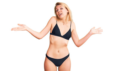 Young beautiful blonde woman wearing bikini clueless and confused expression with arms and hands...