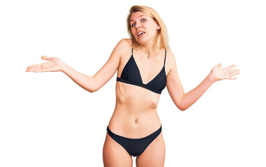 Obraz premium Young beautiful blonde woman wearing bikini clueless and confused expression with arms and hands raised. doubt concept.