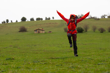 A woman in a red jacket is standing in a field, looking up and smiling