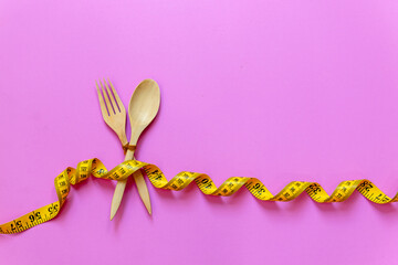 Healthy diet for weight loss. The fork and dish wood wrapped in yellow measuring tape on pink background. Diet and Healthy Concept