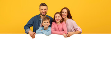 Happy family peeking over a white board