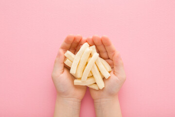 White sticks of potato chips in baby girl opened palms on light pink table background. Pastel color. Closeup. Point of view shot. Top down view.