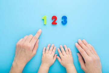 Young mother finger showing colorful numbers to baby. Hands together on light blue table background. Pastel color. Time to learning. Point of view shot. Closeup. Top down view.