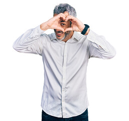 Middle age hispanic with grey hair wearing casual white shirt doing heart shape with hand and fingers smiling looking through sign