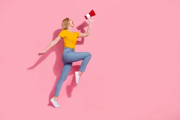 Fotobehang Full length photo of cheerful impressed lady dressed yellow t-shirt jumping high yelling bullhorn empty space isolated pink color background © deagreez