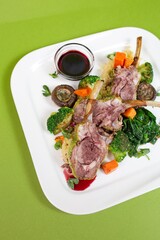 A delicious and healthy rib dish with mushrooms, broccoli, carrots and spinach on a white plate on a green background