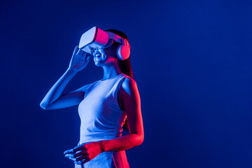 Smart female stand with surrounded by cyberpunk neon light wear VR headset connecting metaverse, futuristic cyberspace community technology. Elegant woman look generated virtual area. Hallucination. - obrazy, fototapety, plakaty