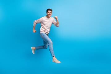 Full body portrait of nice young man jump run empty space wear beige sweatshirt isolated on blue...