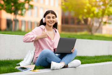 Girl giving thumbs up with laptop outside