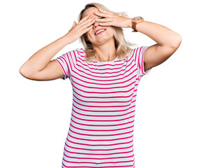 Young caucasian woman wearing casual clothes covering eyes with hands smiling cheerful and funny. blind concept.