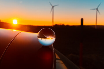 Crystal ball sunset with wind power plant silhouettes and reflections on a car roof near Kugl,...