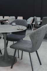 Gray wooden table combined with dark gray wooden chairs with soft fabric upholstery. There are blue porcelain mugs and saucers on the table