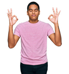 Young handsome hispanic man wearing casual pink t shirt relax and smiling with eyes closed doing meditation gesture with fingers. yoga concept.