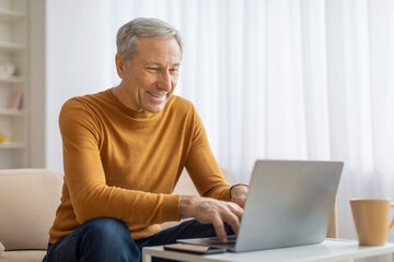 Older man happily working on laptop at home
