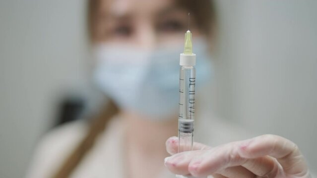 Selective focus image of a healthcare professional's hand holding a syringe, with a blurred background emphasizing the medical instrument