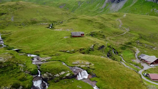 Drone view of green rocky landscape in Alpine hamlet with mountain creeks and wooden cottages